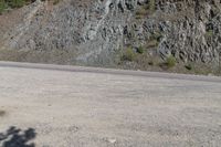 an empty road in the middle of a mountain area near a cliff, with rocks and grass on both sides