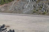 an empty road in the middle of a mountain area near a cliff, with rocks and grass on both sides