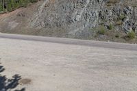 an empty road in the middle of a mountain area near a cliff, with rocks and grass on both sides