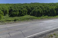 a motorcycle sits on the side of a road, near trees and grass, in front of a hill