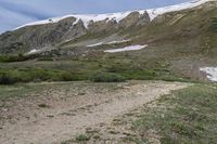 there is an open area with snow on the mountains behind it and a trail leading towards the camera