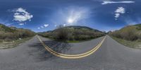 a scenic view of an empty highway taken through a fish eye lens with a blue sky behind it