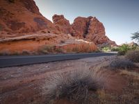 there is a road passing a small mountain side canyon and desert area in front of the mountains