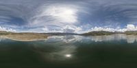 a body of water in the middle of a desert area with clouds reflected in it