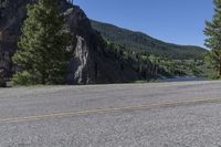 a motorcycle is traveling on the highway next to a mountain pass through the forest with a view of a river and cliffs