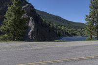 a motorcycle is traveling on the highway next to a mountain pass through the forest with a view of a river and cliffs