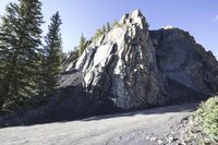 rock formation near the side of a mountain near pine trees near road, outdoors in outdoor