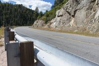 a motorcycle leaning against the railing of a mountain pass that has rocky cliff and trees on it