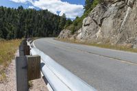 a motorcycle leaning against the railing of a mountain pass that has rocky cliff and trees on it