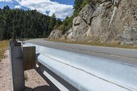 a motorcycle leaning against the railing of a mountain pass that has rocky cliff and trees on it