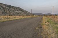 a lone paved road stretches into a distant mountain range below power lines and utility poles