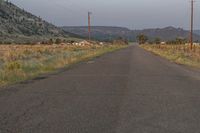 a lone paved road stretches into a distant mountain range below power lines and utility poles