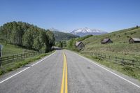 a mountain range is seen behind a long road leading up to it with a fence surrounding and a road sign