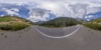 a panorama panoramic view of a mountain range and road with trees and clouds