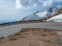 a snow covered road is near a very steep cliff on a clear day the wall is filled with snow and snow