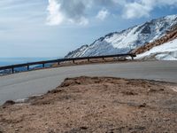 a snow covered road is near a very steep cliff on a clear day the wall is filled with snow and snow