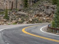 the curved road curves in front of a mountain area with pine trees behind it,