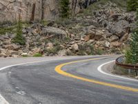 the curved road curves in front of a mountain area with pine trees behind it,