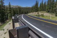 a curved highway with yellow line on the side in the mountains with pine trees in the foreground