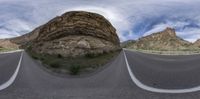 a photo with a curved road going through it and mountains and sky with clouds in the background