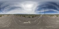 an 360 view from below of a dirt road with mountains in the background and clouds above