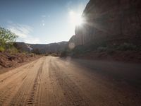 sun flares above a dusty dirt road through a mountainous setting on a sunny day