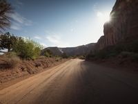 sun flares above a dusty dirt road through a mountainous setting on a sunny day