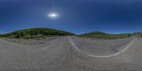 a 360 camera photograph of a empty mountain road and forest scene in motion with lens pointed slightly into the air