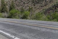 an empty street near some mountain side with yellow lines and some trees behind it to the left