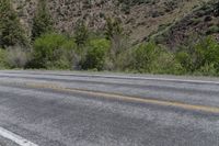 an empty street near some mountain side with yellow lines and some trees behind it to the left