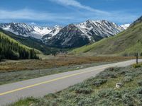 the road is paved with yellow markings and has a snowy mountain range in the background