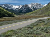 the road is paved with yellow markings and has a snowy mountain range in the background