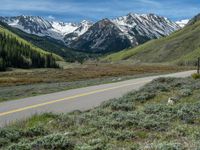 the road is paved with yellow markings and has a snowy mountain range in the background