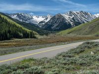 the road is paved with yellow markings and has a snowy mountain range in the background