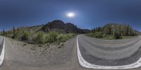 a panoramic view of the long straight road on a sunny day with the sun over a mountain