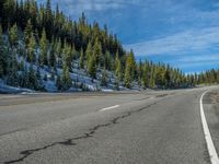 a curve on a road with a snow covered mountain behind it and trees on the left side