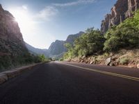 a road going through mountains with trees in the foreground and the sun shining down on them