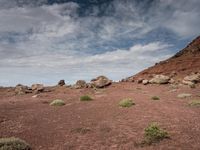 a group of large rocks in a barren desert area with some blue skies overhead and clouds above them