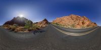 a fish eye lens view of the road through the mountains with sun shining in the sky