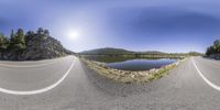 three roads that are near water and rocks in the middle of the road, with sun shining on a large body of water