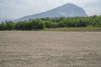 an empty field in front of mountains with trees in the distance and an open area of dirt