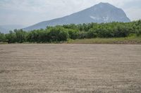 an empty field in front of mountains with trees in the distance and an open area of dirt