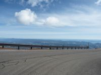 an empty road and a hill overlook the view of mountains and clouds and blue sky