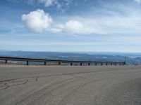 an empty road and a hill overlook the view of mountains and clouds and blue sky