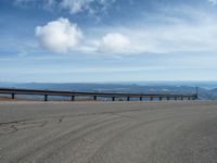 an empty road and a hill overlook the view of mountains and clouds and blue sky