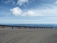 an empty road and a hill overlook the view of mountains and clouds and blue sky