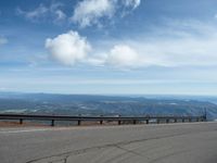 an empty road and a hill overlook the view of mountains and clouds and blue sky