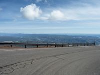 an empty road and a hill overlook the view of mountains and clouds and blue sky