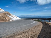 a man is riding his bike down a mountain road with snow and rocks in the background