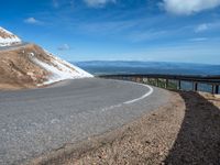 a man is riding his bike down a mountain road with snow and rocks in the background